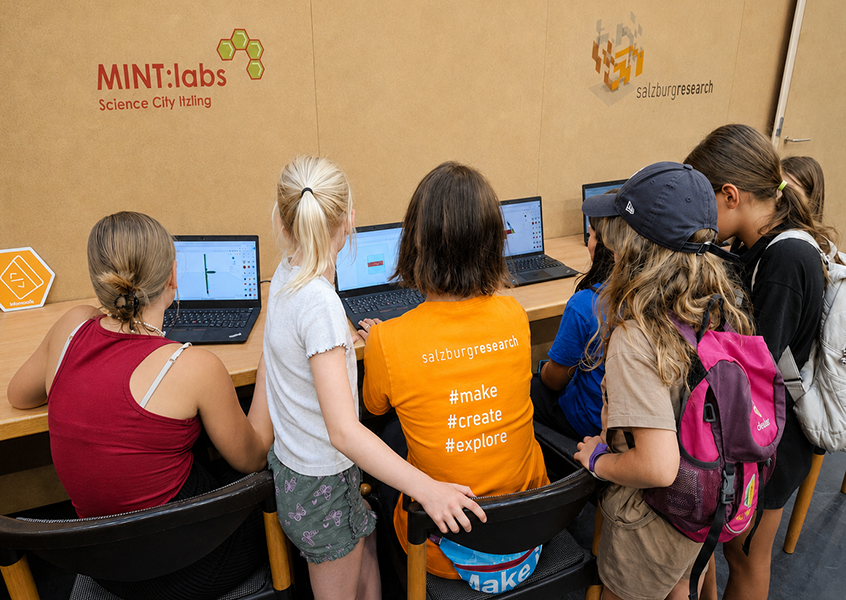 Kinder und Jugendliche arbeiten gemeinsam an mehreren Laptops bei einem 3D-Druck-Workshop der MINT:labs Science City Itzling und Salzburg Research. Mit Hilfe von KI optimiert.